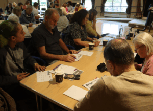 A group sat on a table with pens and note pads infron tof them while they are engaging with the talk.